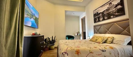 A modern hotel room with a large bed, a flat-screen TV, a dark-colored dresser, and a painting on the wall.