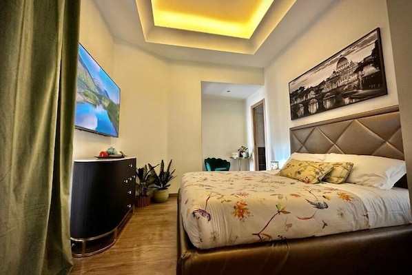A modern hotel room with a large bed, a flat-screen TV, a dark-colored dresser, and a painting on the wall.