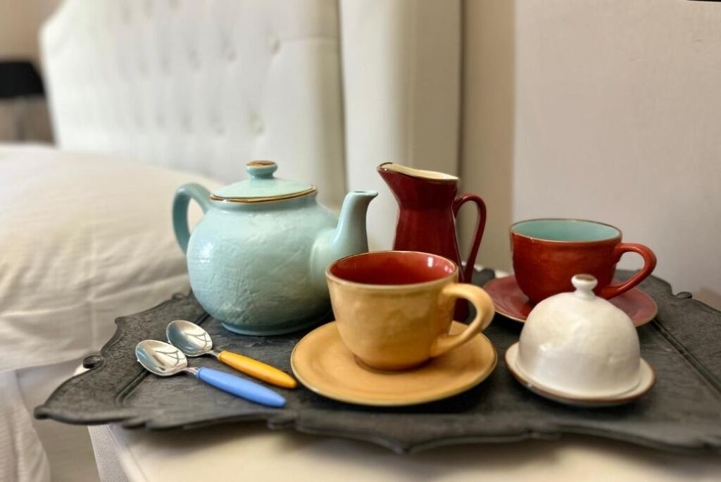 A tray with a blue teapot, a red pitcher, a red cup, a yellow cup, a white cup, and a white lid on a dark surface.