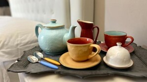 A tray with a blue teapot, a red pitcher, a red cup, a yellow cup, a white cup, and a white lid on a dark surface.