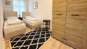 Un dormitorio con dos camas, un armario de madera, una mesita y una alfombra estampada.