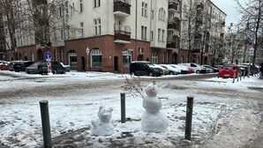 Un muñeco de nieve en un estacionamiento, con edificios al fondo.
