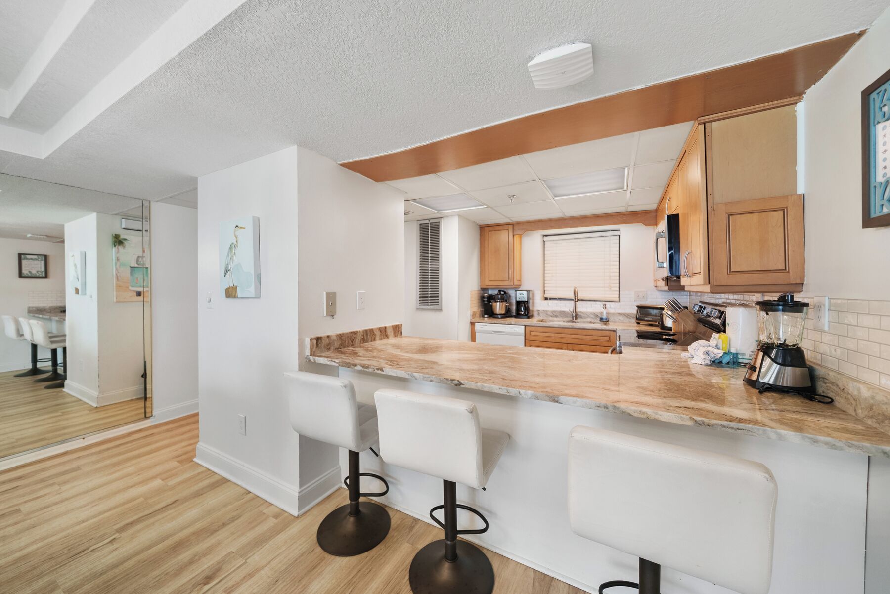 A modern kitchen with a marble countertop, wooden cabinets, and a built-in island with bar stools.