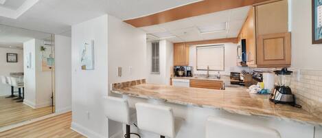 A modern kitchen with a marble countertop, wooden cabinets, and a built-in island with bar stools.