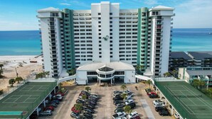 A high-rise hotel with multiple floors, a central entrance, and a parking area with several cars. - Unbeatable Views in this 3BR 3BA Condo at the Watercrest w/Beach Chairs! (Panama City Beach)