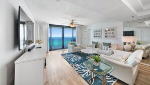 A modern living room with a large window overlooking the ocean, a ceiling fan, and a glass coffee table. - Unbeatable Views in this 3BR 3BA Condo at the Watercrest w/Beach Chairs! (Panama City Beach)