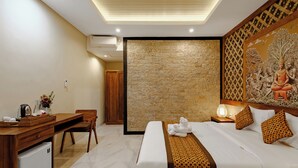 A hotel room with a bed, a desk, a chair, a small refrigerator, a nightstand with a lamp, and a decorative wall panel. - Ray Guest House  (Ubud)