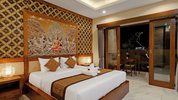 A large bed with white linens, a wooden headboard, and a decorative wall panel. - Ray Guest House  (Ubud)