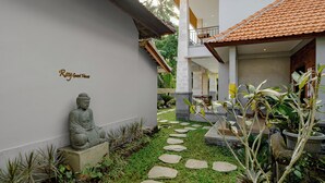A serene courtyard with a Buddha statue, a stone pathway, and lush greenery. - Ray Guest House  (Ubud)