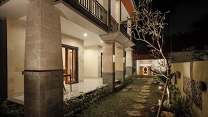 A well-lit outdoor area with a stone pathway leading to a wooden door, surrounded by greenery and decorative lighting. - Ray Guest House  (Ubud)