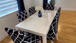 Un comedor con una mesa blanca y sillas de estampado blanco y negro, un florero con flores blancas y un reloj en la pared.