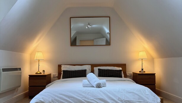 Un dormitorio con una cama grande, dos mesitas de noche con lámparas, un candelabro en el techo y un espejo en la pared.