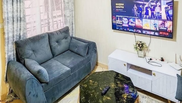 A living room with a grey sofa, a glass coffee table, and a flat-screen TV mounted on the wall displaying 'Queen South'. - The Attic Place South B (Nairobi)