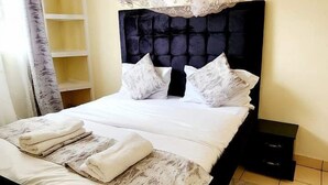 A neatly made bed with a canopy, a bedside table, and a shelf unit in a room with tiled flooring. - The Attic Place South B (Nairobi)