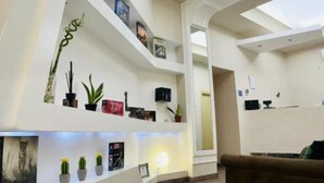 Ein modernes Interieur mit weißer Farbgestaltung, inklusive einer Couch, einem Couchtisch und einem Bücherregal mit verschiedenen Dekorationsobjekten und Büchern.