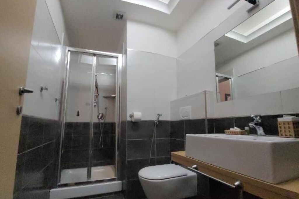 A modern bathroom with a glass-enclosed shower, a white toilet, and a large mirror above the sink.