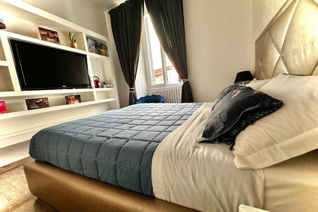 A bedroom with a bed, a TV on a shelf, and a window with curtains.