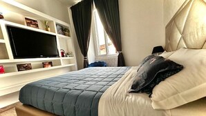 A bedroom with a bed, a TV on a shelf, and a window with curtains.