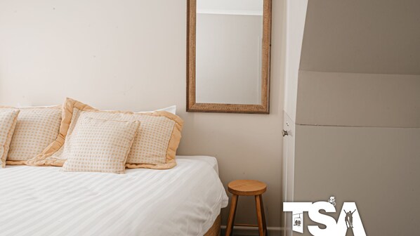 Une chambre à coucher avec un lit, des oreillers, un tabouret en bois et une porte.