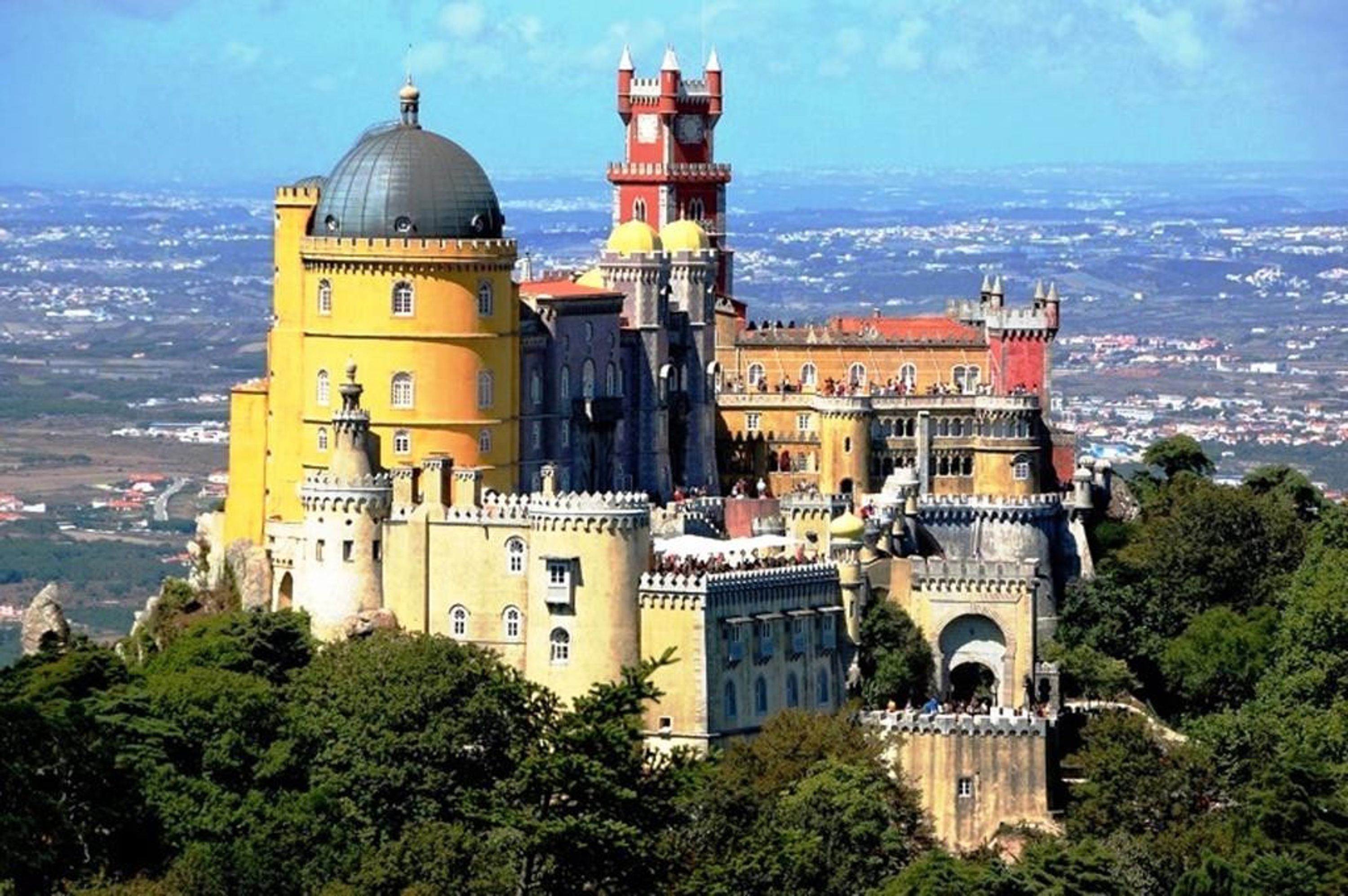 Un castillo grande e histórico con múltiples torres y cúpulas, rodeado de abundante vegetación.