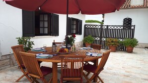 A round wooden table set for six with matching chairs, a red umbrella overhead, and potted plants around. - Cottage Sete Mares in Praia das Ma s (Sintra)