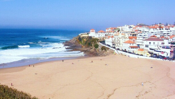 A beach with a rocky shoreline and buildings with red roofs. - Cottage Sete Mares in Praia das Ma s (Sintra)