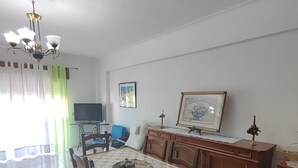 Een eetruimte met een houten tafel en stoelen, een kroonluchter, een televisie en een lijst met een afbeelding aan de muur.