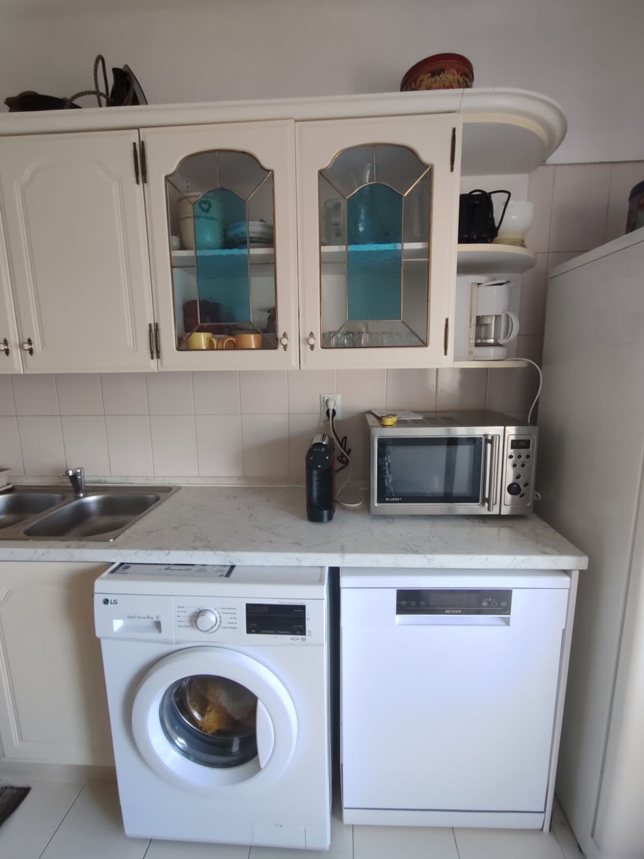 A compact kitchen with white cabinets, a microwave, a coffee maker, and a washing machine.