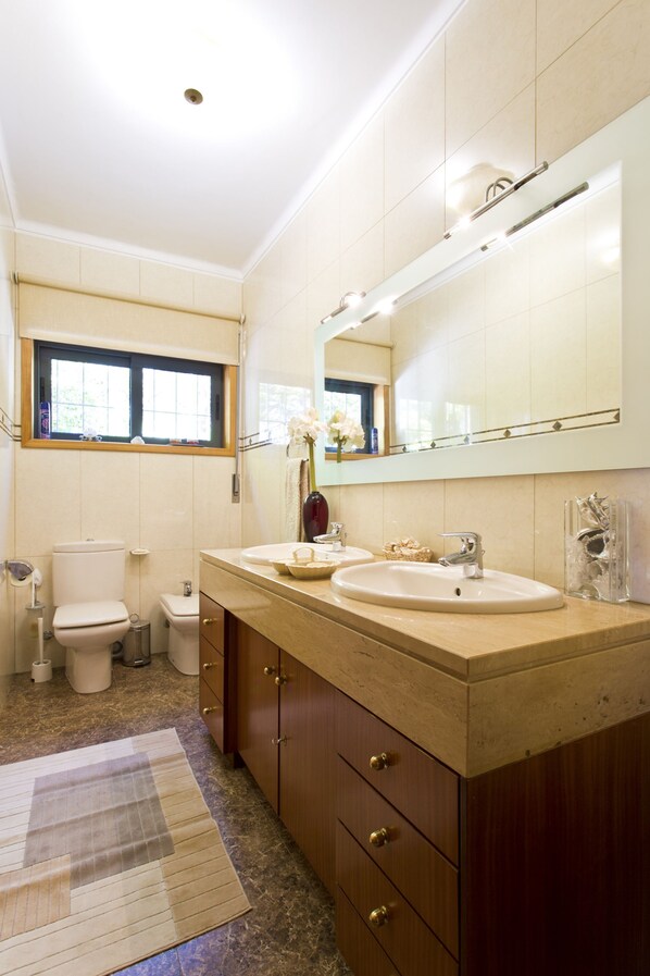 Un baño con dos lavamanos, un inodoro, una ventana y un espejo.
