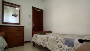 Un dormitorio con un aparador de madera, una cama con colcha floral, una puerta de madera y un espejo decorado con motivos náuticos.