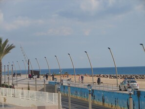 En kystpromenade med gadelamper, en strand og en bil parkeret ved vejen.