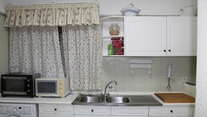 Cocina compacta con lavadora, dos microondas, un fregadero y un armario con un bol y jabón para lavar platos.