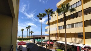 A hotel courtyard with outdoor seating, palm trees, and a view of the ocean.