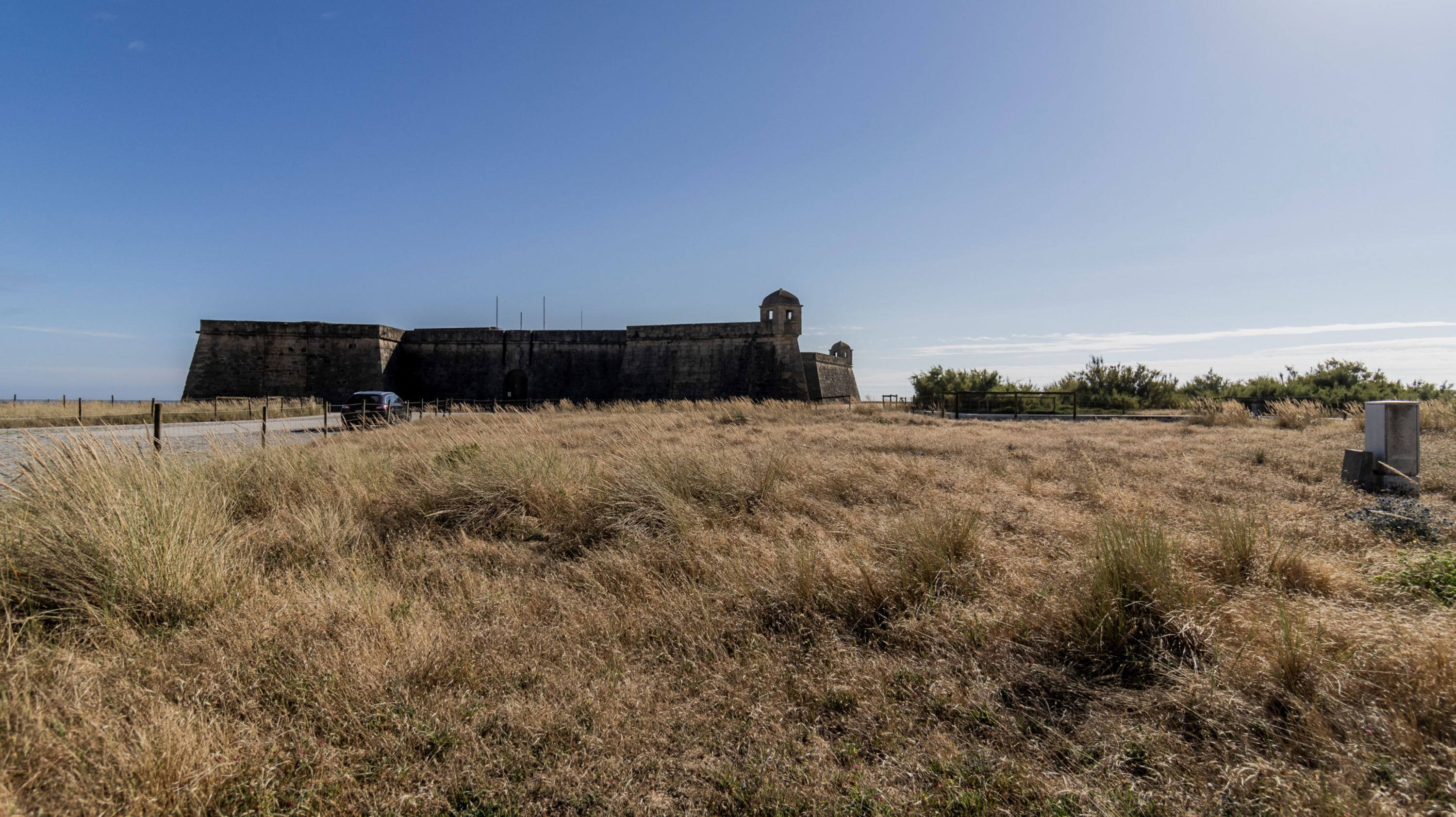 A large, historic stone fort with a watchtower, surrounded by dry grassland and a clear sky.