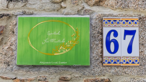 A green sign with 'Quintinha São Martinho' and 'Alojamento Local | Eventos' text, and a blue and white numbered sign '67'.