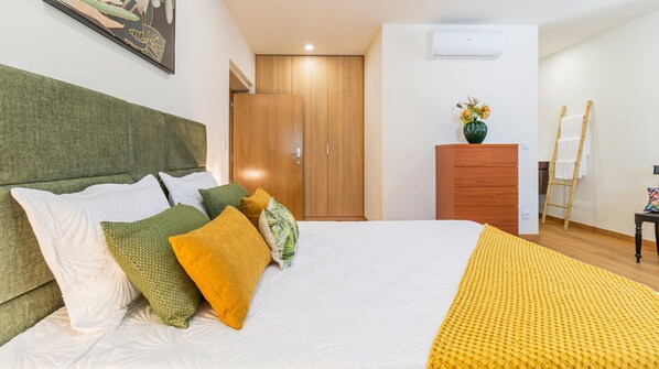A neatly arranged bedroom with a bed, pillows, a dresser, and a painting on the wall.