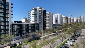 A modern urban residential area with high-rise apartment buildings, a main road with parked cars, and a clear sky. - Nice Flat in Quarteira Beach (Loulé)