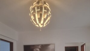 Ett modernt vardagsrum med en stor, platt-TV som är monterad på väggen, ett vitt avlastningsbord med dekorativa föremål och en unik, sfärisk taklampa.