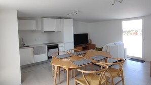 Une cuisine moderne avec des meubles blancs, une table à manger avec des chaises et une grande fenêtre qui laisse entrer la lumière naturelle.