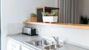 A modern kitchen with a built-in washing machine, a toaster, and a wooden shelf with potted plants.
