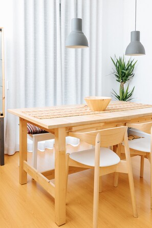 A wooden dining table with a woven placemat, two chairs, and a bowl.