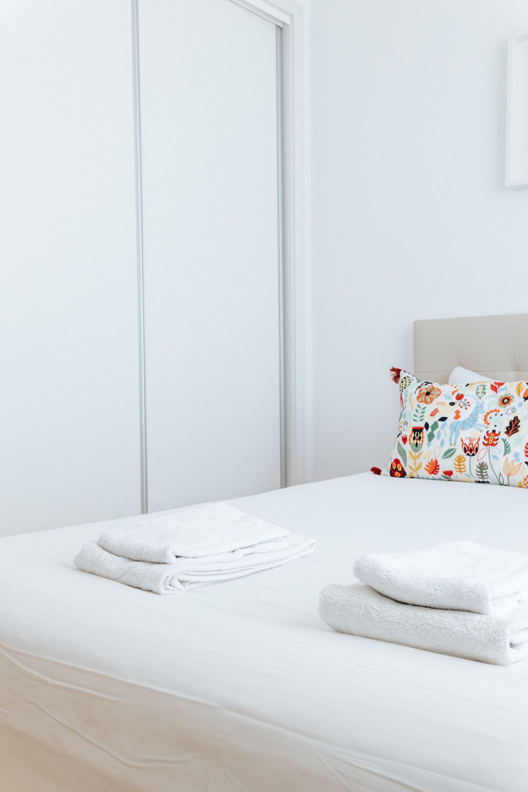 A neatly made bed with white linens and a colorful floral pillow.