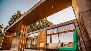 A modern outdoor seating area with wooden flooring, a covered section, and a glass wall. - Deluxe Private Pool Bungalow (Celorico de Basto)