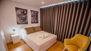 A modern bedroom with a bed, a nightstand, a chair, and curtains. - Deluxe Private Pool Bungalow (Celorico de Basto)