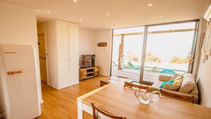 A modern kitchen with a dining area, a TV, and a sliding glass door leading to an outdoor deck. - Deluxe Private Pool Bungalow (Celorico de Basto)
