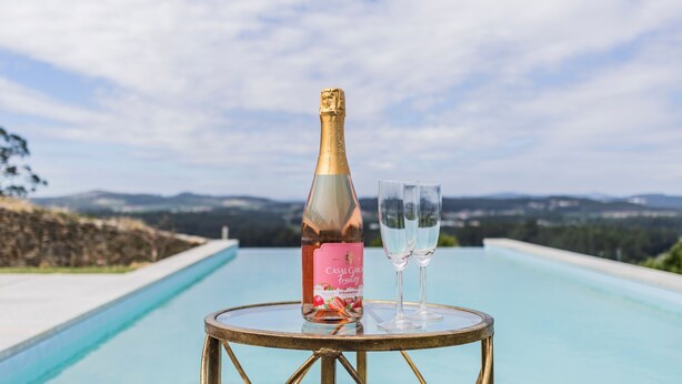 A bottle of Casal Garofalo Fruitzy champagne and two glasses on a round table by a pool with a scenic view. - Quintinha S o Martinho Luxury 2 Suites Villa Eira (Vila do Conde)