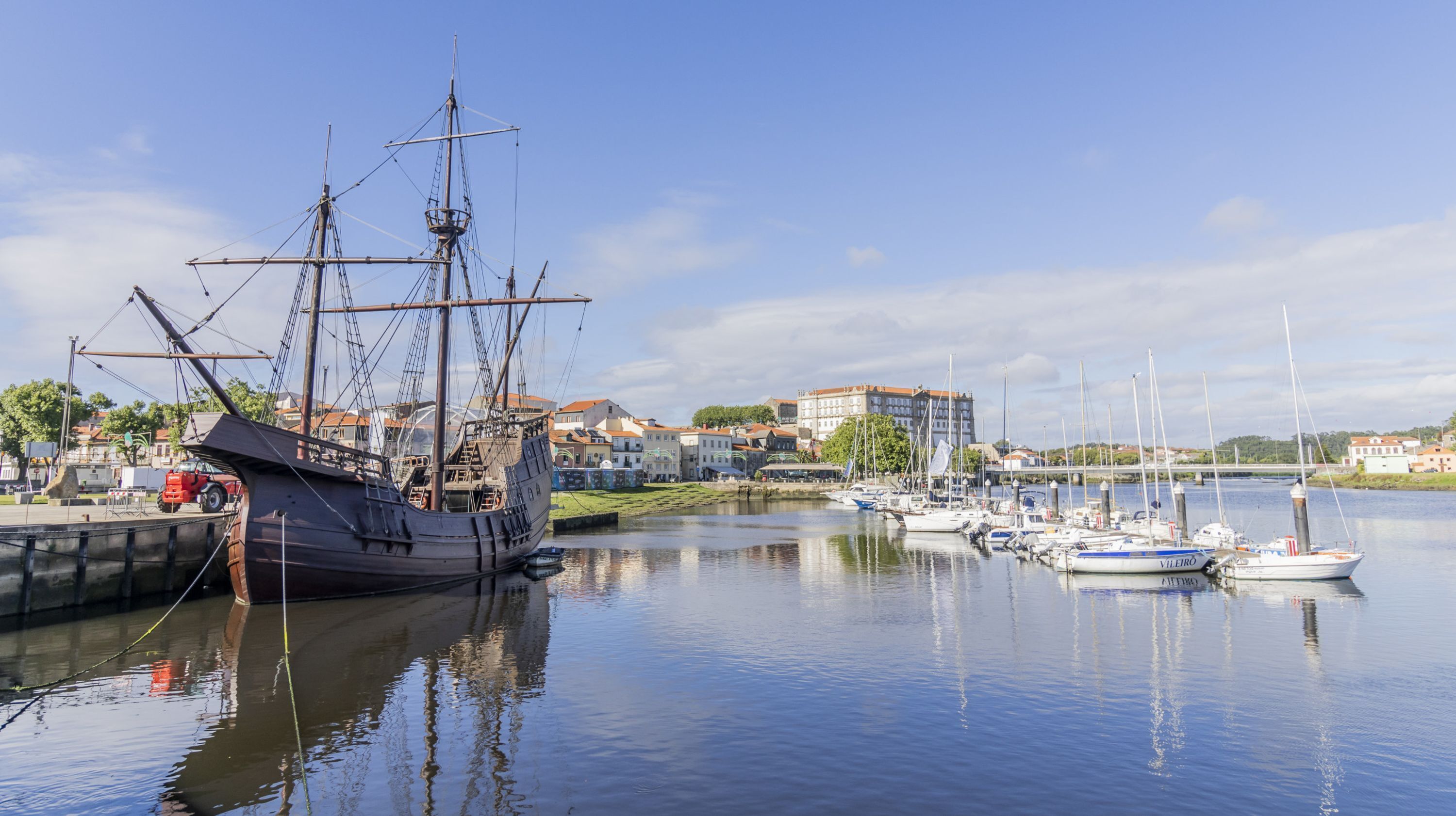 A harbor with a large sailing ship docked, surrounded by calm water and several smaller boats.