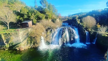 A waterfall cascading over rocks into a river, surrounded by trees and a small building.