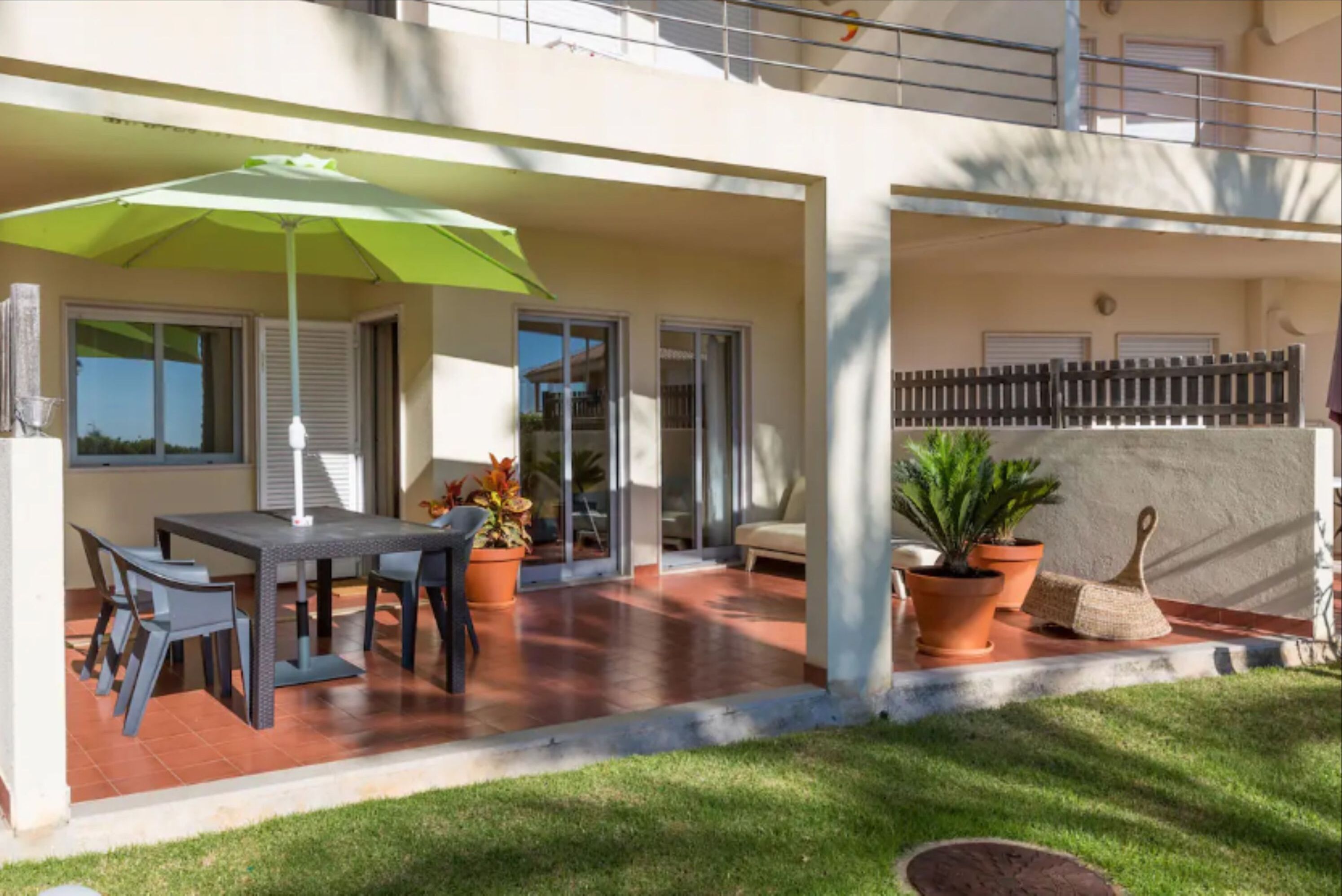 A covered patio with a table and chairs, a green umbrella, and potted plants.