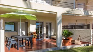 A covered patio with a table and chairs, a green umbrella, and potted plants. - Albufeira Terrace Pool Garage Dream Flat (Albufeira)